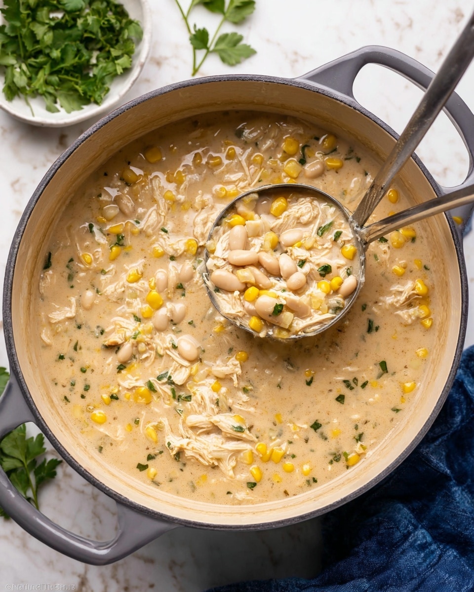 A thick, creamy soup filled with shredded white chicken, yellow corn kernels, and white beans is shown inside a round gray pot with a white inside. The soup is pale beige with specks of green herbs throughout. A metal ladle scoops some of the soup, showing the chunky texture of the ingredients mixed in the creamy broth. The pot sits on a white marbled surface with some green herbs and a white bowl with greens nearby, and a blue cloth is partially visible at the bottom right corner. Photo taken with an iphone --ar 4:5 --v 7