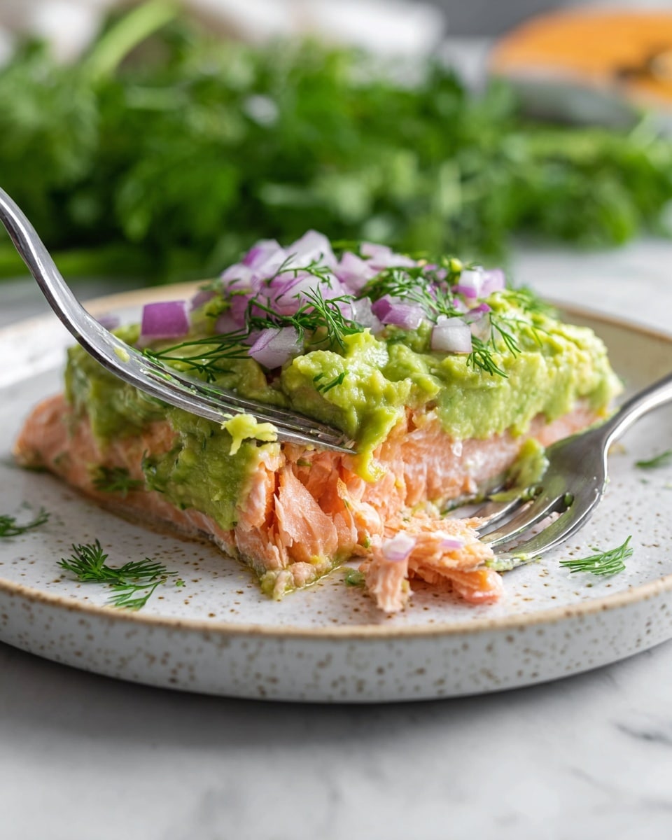 A piece of cooked salmon fillet with light pink and slightly crispy edges lies on a white speckled plate. On top of the salmon is a thick layer of mashed green avocado mixed with finely chopped red onions and small sprigs of fresh green dill, giving it a textured and fresh look. A silver fork presses gently into the avocado and salmon layers, causing some of the soft fish to break off slightly on the plate. The plate is placed on a white marbled surface with a blurred green background suggesting fresh herbs. photo taken with an iphone --ar 4:5 --v 7