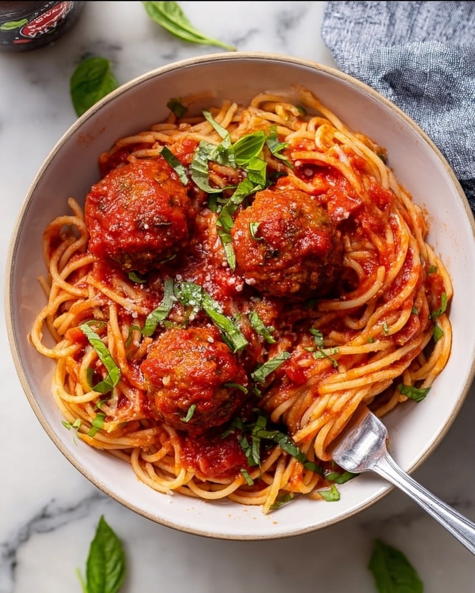 A white bowl filled with spaghetti noodles coated in red tomato sauce, with three large round meatballs placed on top evenly; the meatballs are covered in sauce and small tomato pieces. Fresh green basil leaves and chopped herbs are scattered over the spaghetti and meatballs, adding pops of bright green color. A fork rests inside the bowl on the left side, and the bowl sits on a white marbled surface with a few loose basil leaves nearby. photo taken with an iphone --ar 4:5 --v 7