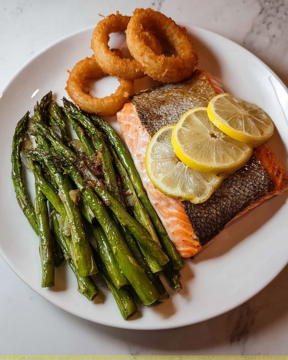 A white round plate holds a meal arranged in three parts: on the right side is a large piece of cooked salmon with golden-brown, crispy skin on top, and three thin lemon slices placed along the center of the salmon piece, each slice showing delicate segments and seeds. On the left of the salmon is a heap of bright green asparagus spears, slightly charred with a shiny, glistening texture from cooking, some small bits of seasoning visible on them. Above the salmon and asparagus, near the edge of the plate, are three golden-brown onion rings with a light crispy texture. The plate sits on a white marbled surface. photo taken with an iphone --ar 4:5 --v 7