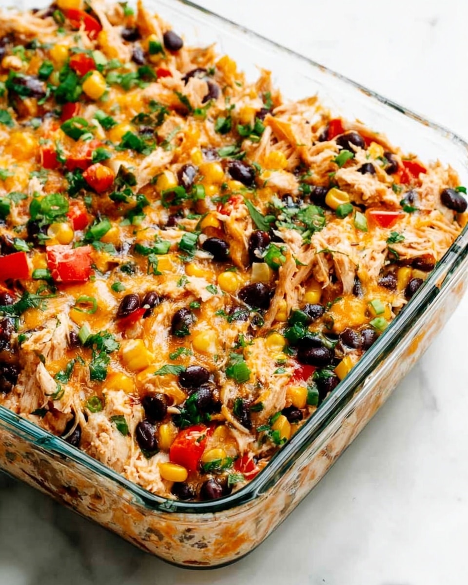 A clear glass baking dish filled with a mixed layered dish showing shredded cooked chicken mixed with melted cheese, black beans, yellow corn, diced red bell peppers, and chopped green onions and herbs sprinkled on top. The textures include the soft, shredded chicken and melted cheese combined with the smooth beans and tender corn, all mixed evenly across the dish. The colors are warm and vibrant with orange cheese, white chicken, black beans, yellow corn, and green onion pieces creating a fresh and colorful look against the clear glass container, all set on a white marbled surface. Photo taken with an iphone --ar 4:5 --v 7