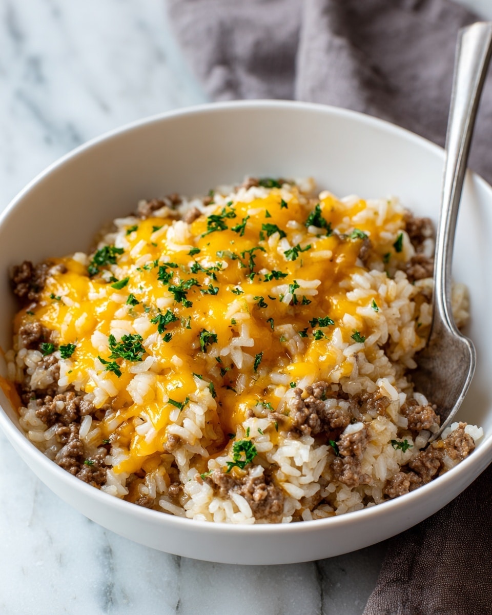 A white bowl filled with a layered dish of cooked white rice mixed with browned ground beef, topped with melted yellow cheddar cheese scattered over the surface, and sprinkled with chopped bright green parsley. The texture shows soft, fluffy rice grains combined with crumbly beef pieces, while the cheese appears gooey and slightly melted. A silver spoon rests inside the bowl on the right side. The bowl is placed on a white marbled surface with a soft gray cloth in the background. Photo taken with an iphone --ar 4:5 --v 7