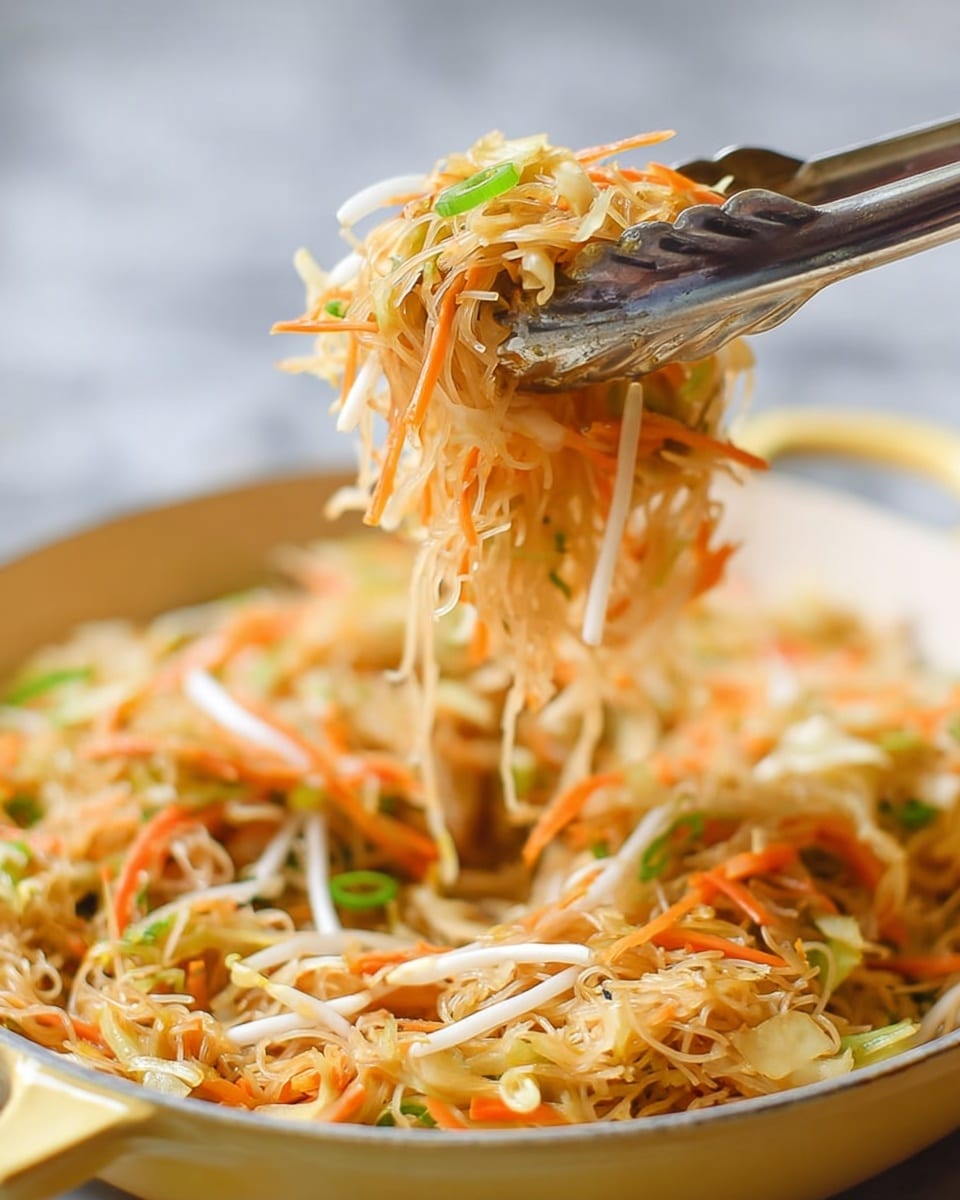 A close-up of stir-fried noodles lifted by silver tongs, showing thin, light brown noodles mixed with shredded orange carrots, white bean sprouts, and thin green onion slices, all in a white bowl with yellow handles on a white marbled surface. The noodles have a slightly glossy texture, and the vegetables add fresh color and crunch throughout the dish. The background is softly blurred, focusing on the food and tongs. photo taken with an iphone --ar 4:5 --v 7