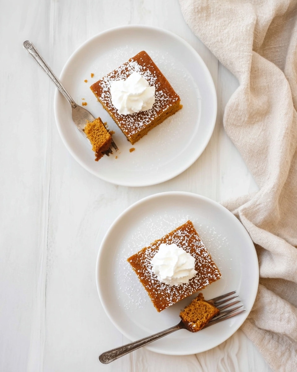 Two white plates sit on a white marbled surface, each holding a single square piece of brown cake with a soft texture. Each cake square has a small dollop of white whipped cream on top and is lightly dusted with powdered sugar. One plate has a fork resting beside the cake, while the other plate shows a fork with a bite-sized piece of cake on it. A beige cloth is softly draped to the side. The scene has a clean, simple look with soft natural light. photo taken with an iphone --ar 4:5 --v 7