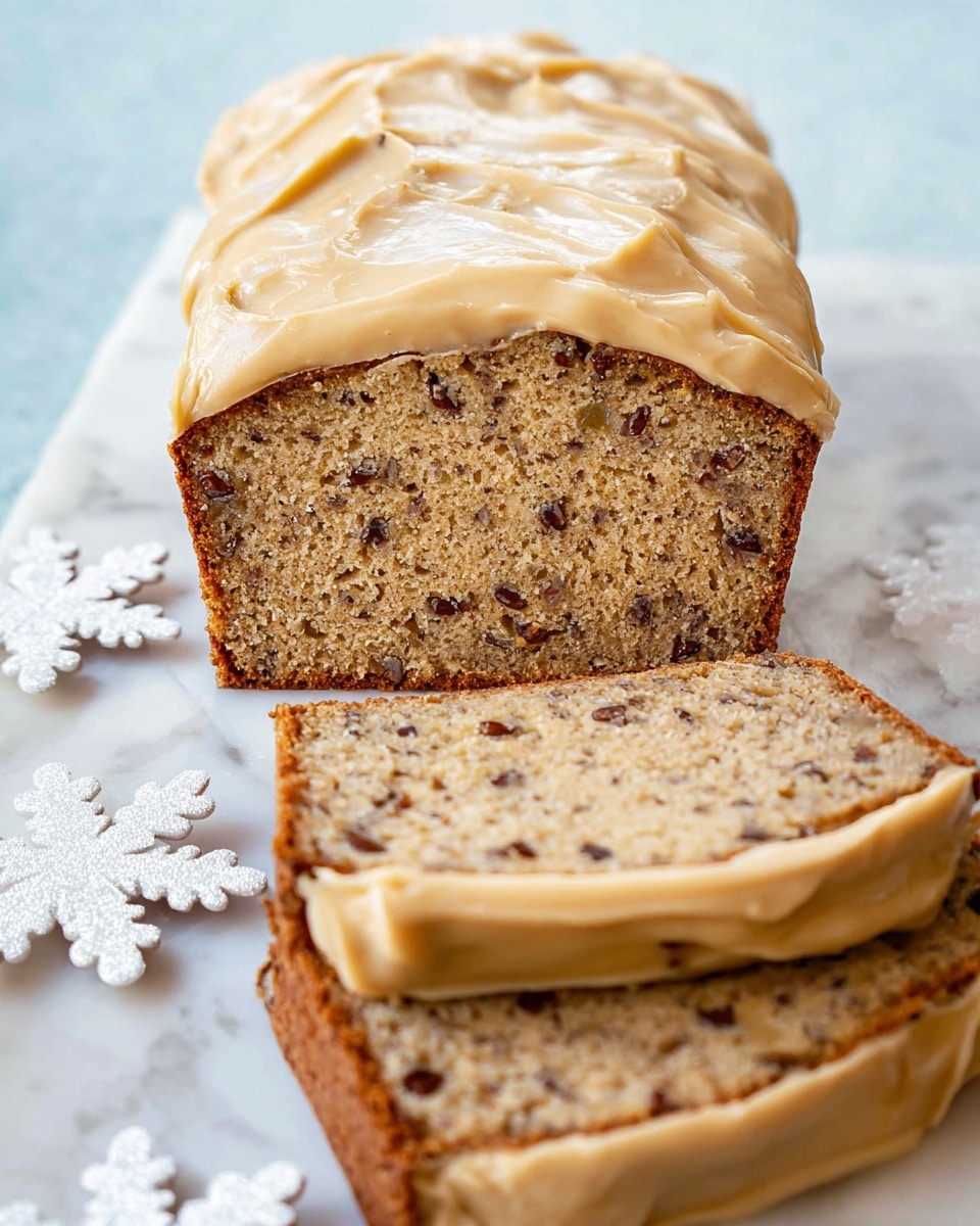 A loaf of nut bread with a light brown crumb filled with small dark nut pieces is shown in close-up. The top layer is covered in a smooth, creamy beige frosting that looks thick and spread evenly over the bread. The bread’s crust is a darker brown, visible around the edges. Three slices lie in front of the loaf, each showing the nut-speckled beige interior and a thin layer of frosting on top. The loaf rests on a white marbled surface decorated with a white snowflake-shaped doily. photo taken with an iphone --ar 4:5 --v 7