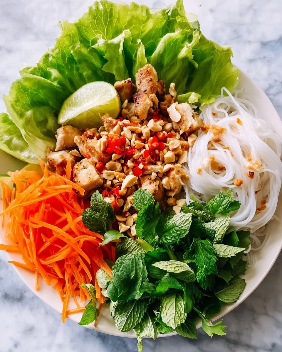 A white plate with thin white noodles on the right side, topped with small red chili pieces. Next to the noodles, a light green wedge of lime rests against fresh crisp lettuce leaves. In the center, there are golden brown grilled chicken pieces sprinkled with crushed peanuts and red chili bits. Surrounding the chicken, shredded orange carrots, a bundle of fresh green mint leaves, light green thinly sliced celery, and fresh dark green cilantro leaves create a colorful ring. The plate sits on a white marbled textured surface. Photo taken with an iphone --ar 4:5 --v 7