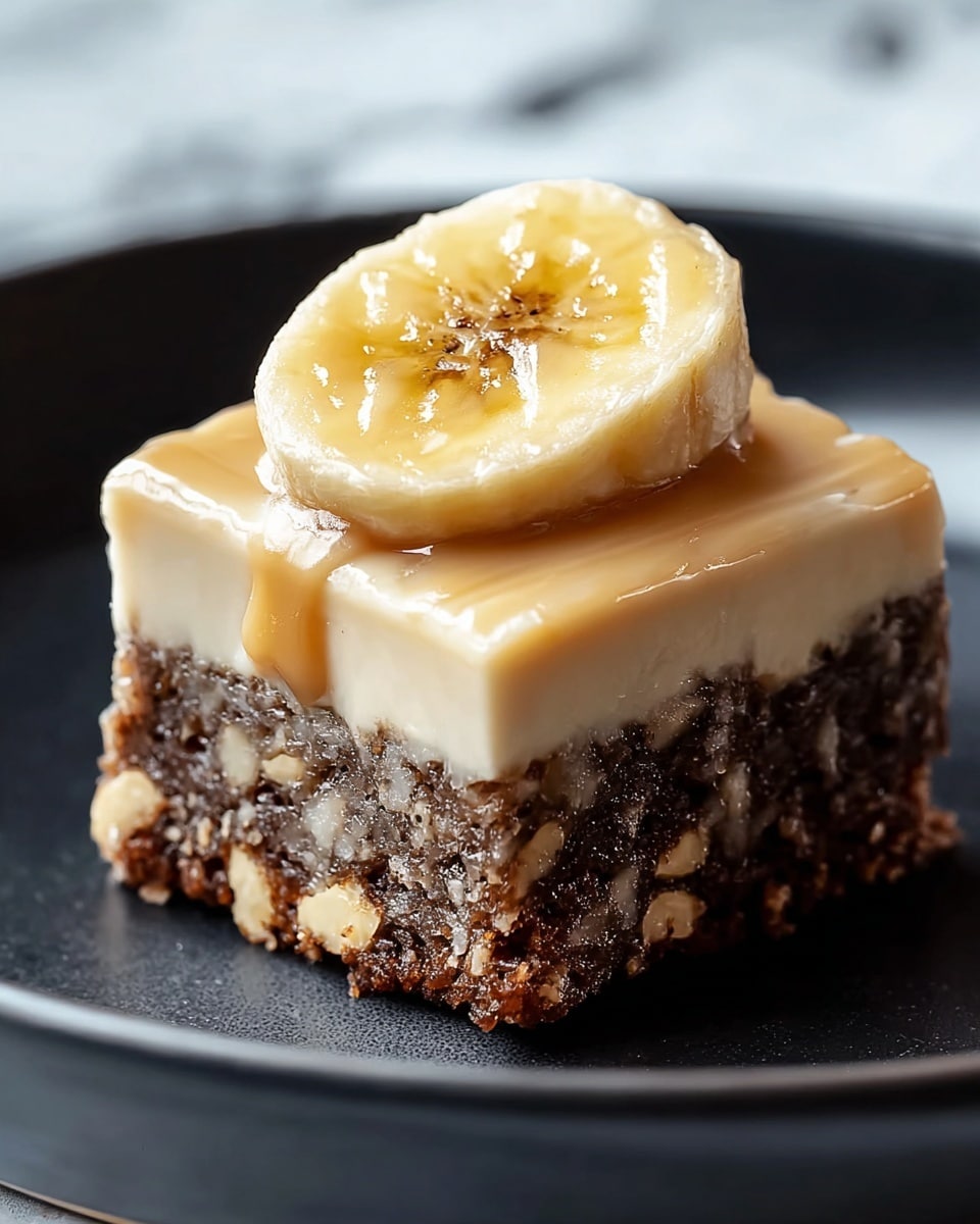 A single square piece of cake is shown with two layers. The bottom layer is dark brown with visible chunks of banana embedded inside, giving it a crumbly texture. The top layer is smooth and creamy, beige in color, evenly spread over the cake. On top of the creamy layer sits a thick, round slice of banana, slightly shiny and moist, with some syrup or glaze on its surface. The cake is placed on a dark plate over a white marbled texture. Photo taken with an iphone --ar 4:5 --v 7