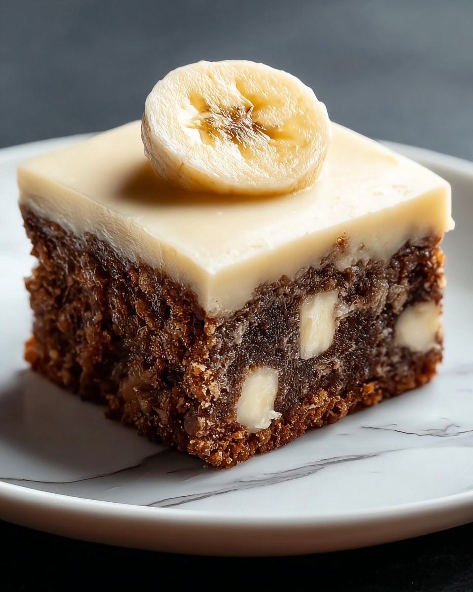 A square piece of dense, dark brown cake with a crumbly texture is shown on a white plate. The cake has visible white banana pieces embedded inside it, giving it a spotted look. On top of the cake is a smooth, thick layer of light cream-colored frosting that covers the entire surface evenly. A round slice of banana with a slightly shiny surface sits upright right in the center on top of the frosting. The plate rests on a white marbled surface. photo taken with an iphone --ar 4:5 --v 7