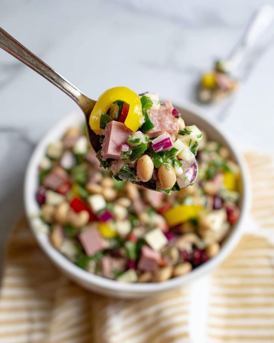 A close-up of a spoon holding a mix of small diced ingredients including light pink cubes of meat, white cheese cubes, light beige beans, green leafy herbs, small pieces of red onion, and a yellow ringed pepper slice on top. In the background, there is a white bowl filled with the same mixed salad, showing more yellow peppers, bits of red, green, white, and beige scattered throughout. The bowl sits on a white marbled surface with a beige and white striped cloth partially visible to the side. The overall look is colorful with a fresh, textured mix of vegetables, legumes, and cheese. Photo taken with an iphone --ar 4:5 --v 7