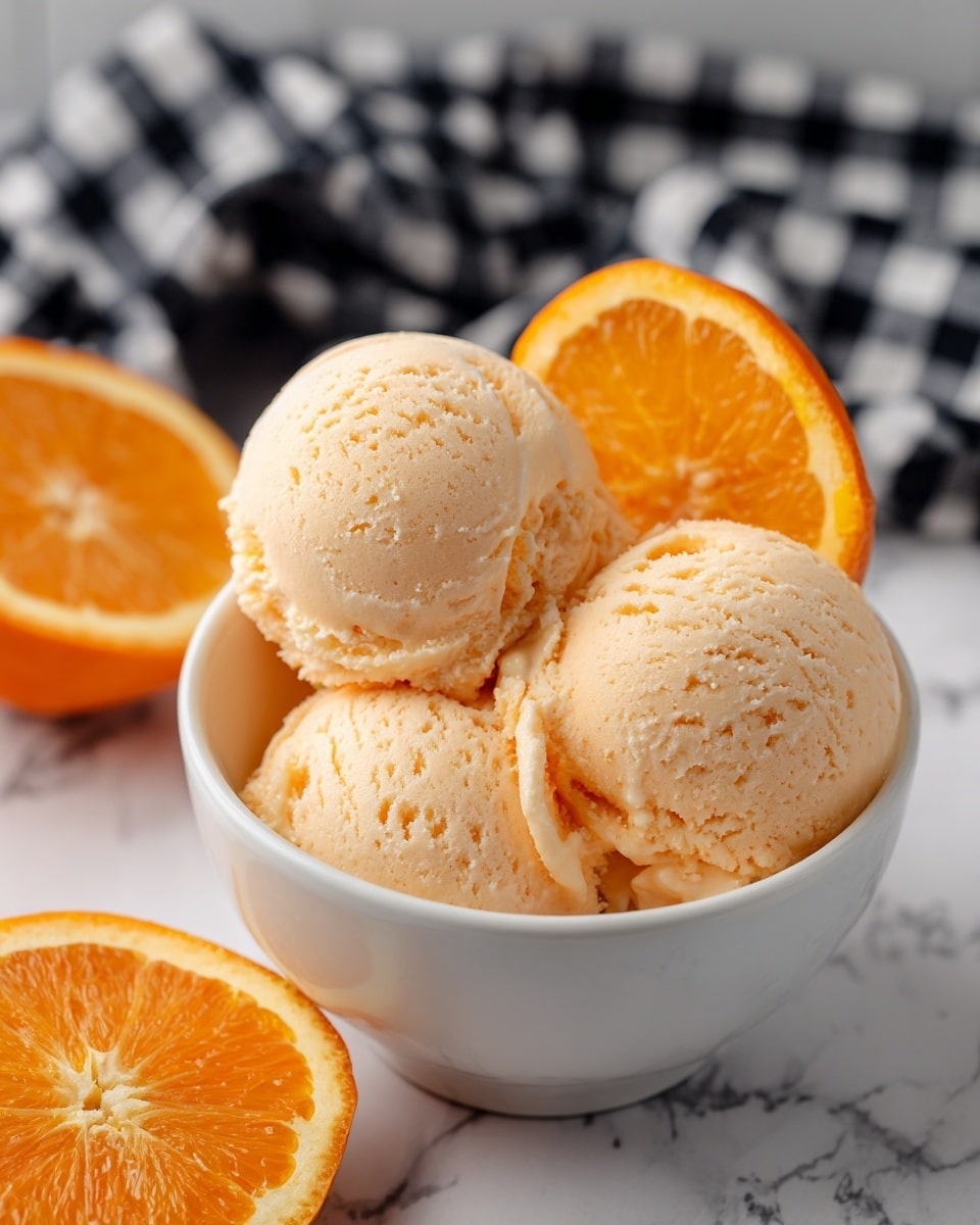A white bowl holds three soft mounds of pale orange sherbet, with one smooth scoop sitting on top in the center; a bright orange slice leans on the side of the bowl behind the sherbet, showing its juicy texture and vivid color. In the background, two orange halves are visible, contrasting with a black and white checkered cloth and a white marbled surface beneath. The sherbet looks creamy and fresh, while the colors of the orange slice and halves add brightness to the scene. photo taken with an iphone --ar 4:5 --v 7