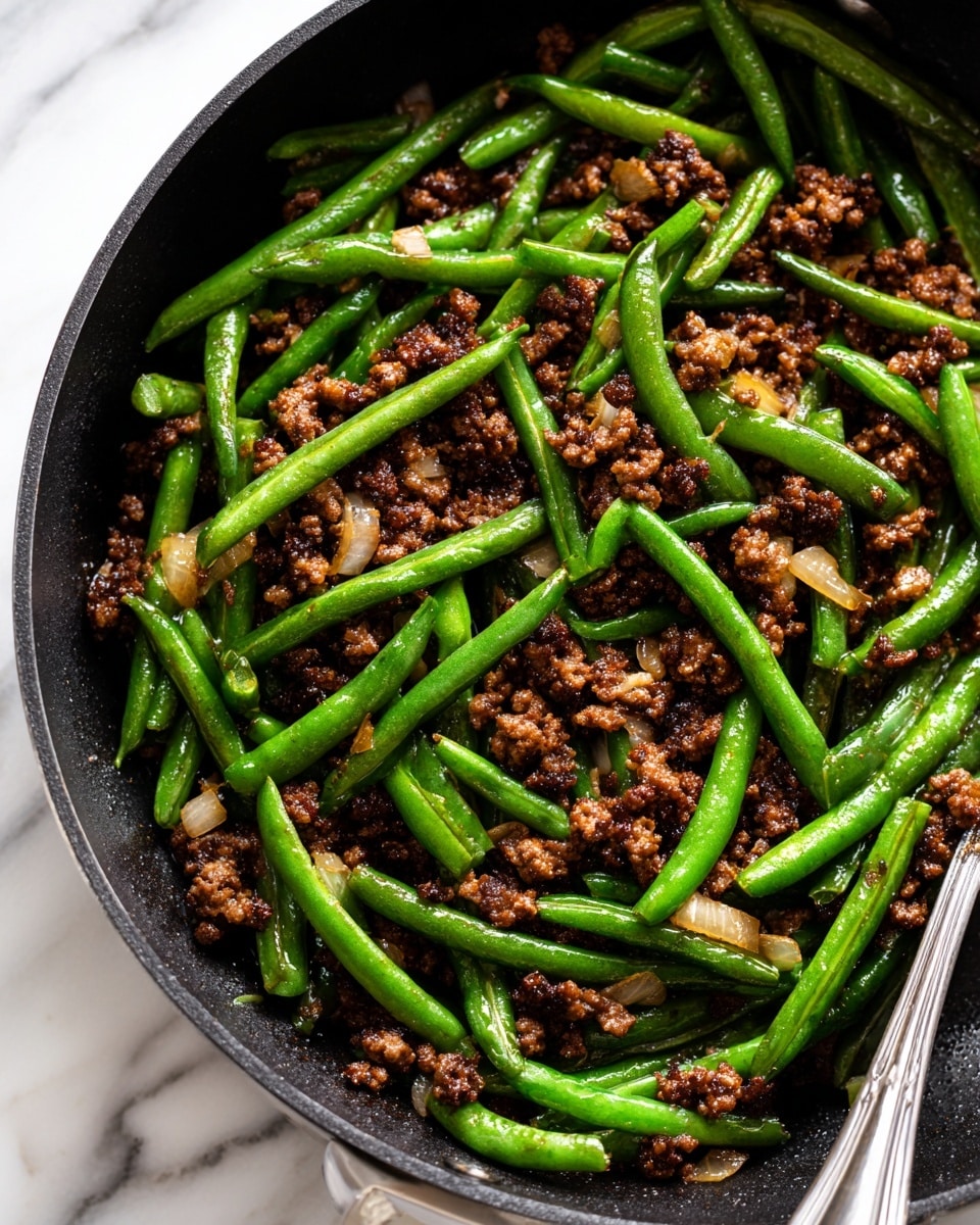 A close-up view of a cooked dish in a black pan showing two main layers mixed together: bright green cooked green beans that look shiny and tender, and small pieces of browned ground meat with a slightly coarse texture, scattered evenly through the green beans. Small bits of cooked onion or vegetable pieces are visible, adding a touch of orange-brown color that contrasts with the green and meat layers. The overall dish looks saucy with a light glaze giving a fresh and appetizing look. Photo taken with an iphone --ar 4:5 --v 7