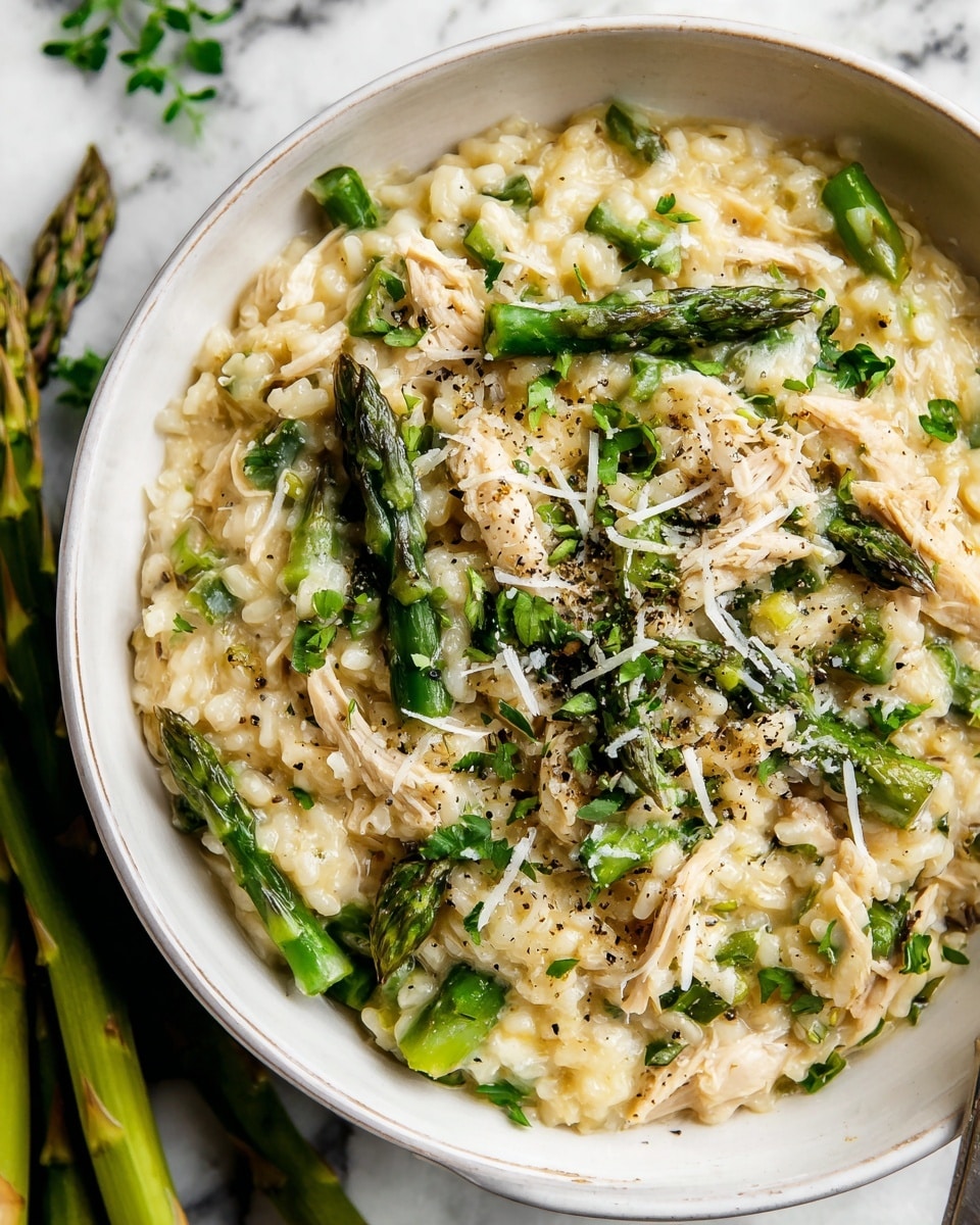 A white bowl filled with a creamy risotto base in light beige, mixed with bright green asparagus pieces and shredded light brown chicken. On top, whole green asparagus spears are laid in a slight mound with a few strands of shredded white cheese sprinkled over, accompanied by finely chopped green herbs and a light dusting of black pepper, all set against a white marbled surface with some asparagus stalks blurred in the background. Photo taken with an iphone --ar 4:5 --v 7