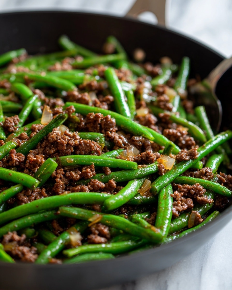 A close-up view of a black skillet filled with cooked green beans and browned ground meat. The green beans are bright green and glossy, scattered evenly throughout the skillet. The ground meat is finely crumbled and dark brown, mixed well with small chunks of cooked onion that are light golden in color. The texture of the green beans is smooth and firm, while the meat looks crumbly and moist. The skillet rests on a white marbled surface, and a silver spoon is partially visible on the right side. photo taken with an iphone --ar 4:5 --v 7