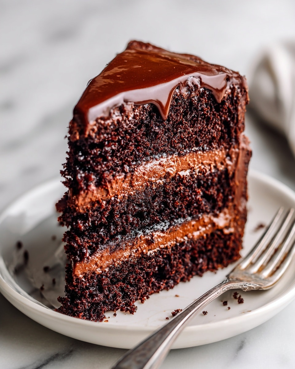 A close-up of a three-layer chocolate cake slice on a white plate showing rich, dark brown soft sponge layers separated by smooth, thick milk chocolate cream filling. The top of the cake is covered with a glossy, dark chocolate ganache that shines under the light. A silver fork rests next to the cake on the plate. The background features a white marbled texture. photo taken with an iphone --ar 4:5 --v 7