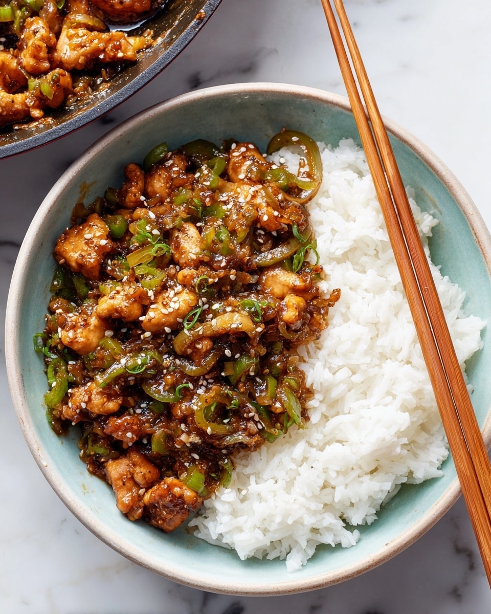 A light blue bowl filled with a base layer of white, fluffy rice, topped with a thick layer of glossy, brown stir-fried chicken pieces mixed with light green celery slices and translucent cooked onions. The chicken has a rich sauce that coats each piece, giving them a slightly shiny, textured look. A pair of light brown wooden chopsticks rests on the right side of the bowl, partially inserted into the dish. The bowl sits on a white marbled surface, with part of a large pan of the same dish visible in the top background. Photo taken with an iphone --ar 4:5 --v 7
