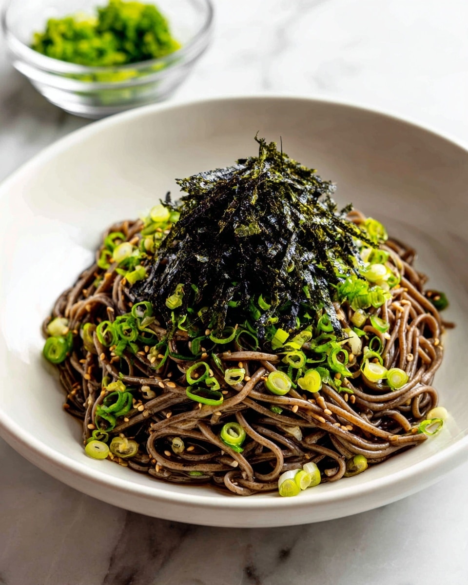 A bowl filled with a single large serving of dark brown soba noodles sits in the center, tossed with small light brown sesame seeds and chopped green onions scattered evenly throughout. On top sits a generous pile of shredded black seaweed, glossy and slightly textured. The noodles and toppings are inside a shiny light gold bowl, placed on a white marbled surface. In the background, there is a blurry glass bowl with green onions and a pair of wooden chopsticks resting on a white cloth. photo taken with an iphone --ar 4:5 --v 7