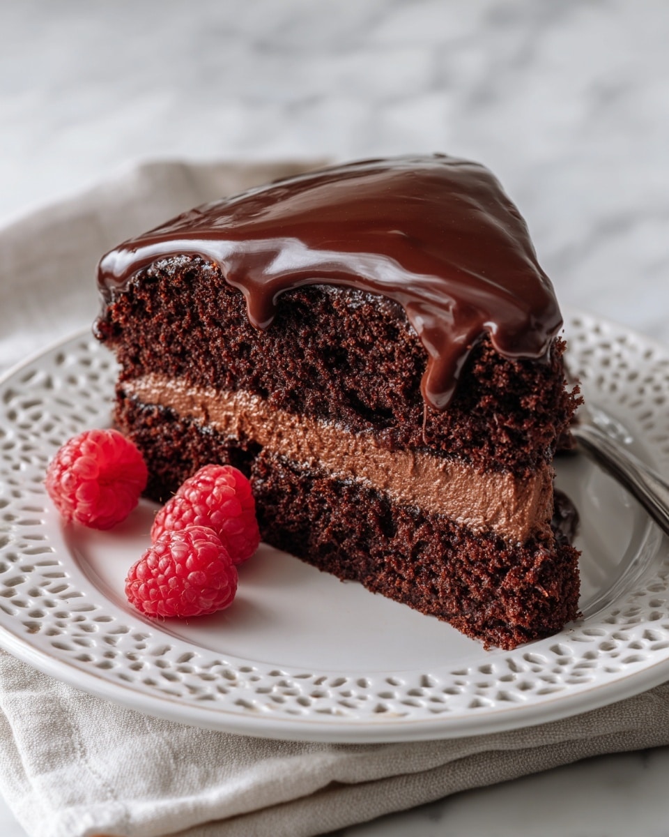 A two-layer chocolate cake sits on a white plate with a delicate lace-like pattern on the edge. The bottom layer is dark brown and moist, topped with a smooth, thick layer of glossy chocolate frosting. The second cake layer is similarly dark and rich, covered with a generous, glossy chocolate frosting that drips slightly over the edges. Two fresh red raspberries rest on the plate beside the cake, adding a bright pop of color. The background is a soft, white marbled texture, creating a clean and elegant setting. photo taken with an iphone --ar 4:5 --v 7