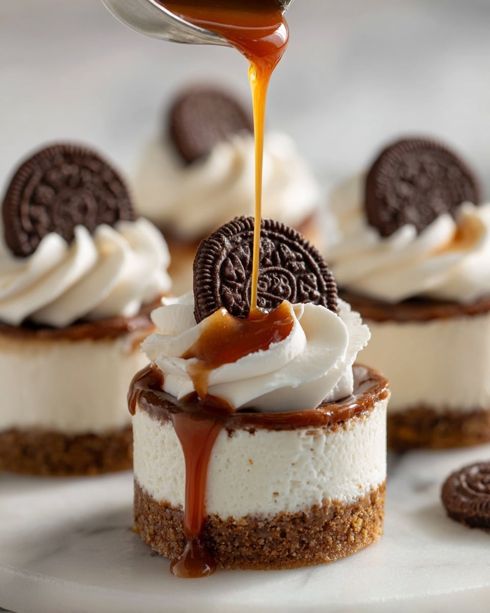 The image shows five small round cheesecakes on a white marbled surface, each with three visible layers: a crumbly golden-brown base, a thick creamy white middle layer, and a swirl of white whipped cream on top. Caramel sauce is being poured over the swirl of whipped cream on the nearest cheesecake, dripping down the sides. Each whipped cream swirl has a round chocolate piece with a detailed pattern placed on top. The background is softly blurred, showing a kitchen setting. photo taken with an iphone --ar 4:5 --v 7