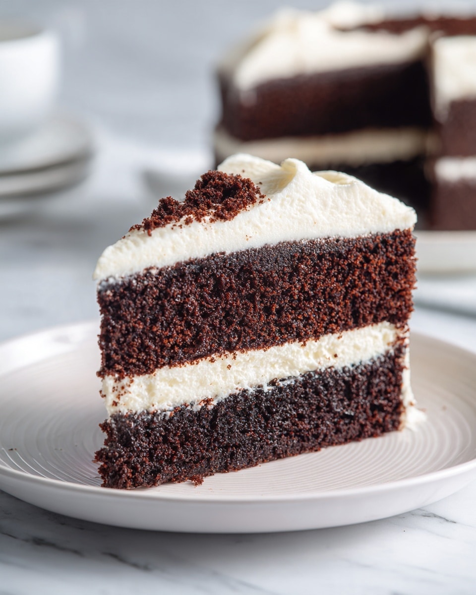 A slice of two-layer chocolate cake sits on a white plate, each chocolate layer looking moist and crumbly with a rich dark brown color. Between the two cake layers is a thick layer of smooth, creamy white frosting that also covers the top of the cake, spreading evenly with a slightly glossy texture. There is a small crumb of the chocolate cake resting on the top of the frosting. The background is a soft, white marbled surface, adding a clean and simple look to the scene. photo taken with an iphone --ar 4:5 --v 7