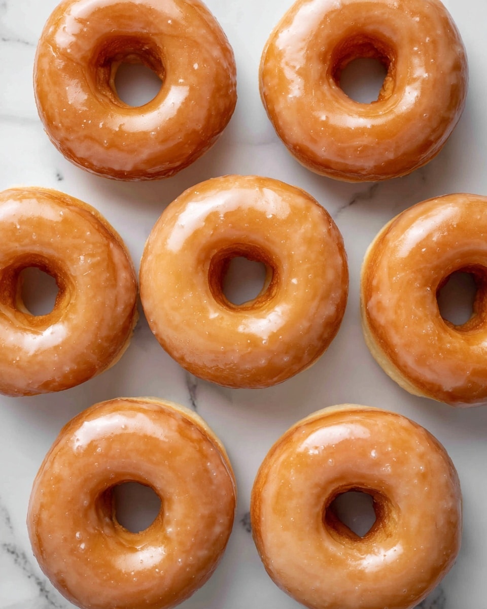 Nine glazed donuts are arranged in a close, neat grid on a white marbled surface. Each donut has a shiny, golden-brown color with a smooth, sticky glaze that catches the light, giving them a slightly wet look. The donuts have a consistent round shape with a hole in the center, and their soft texture is visible under the glaze. The image focuses on the donuts without any other objects or colors, creating a clean and simple presentation. photo taken with an iphone --ar 4:5 --v 7
